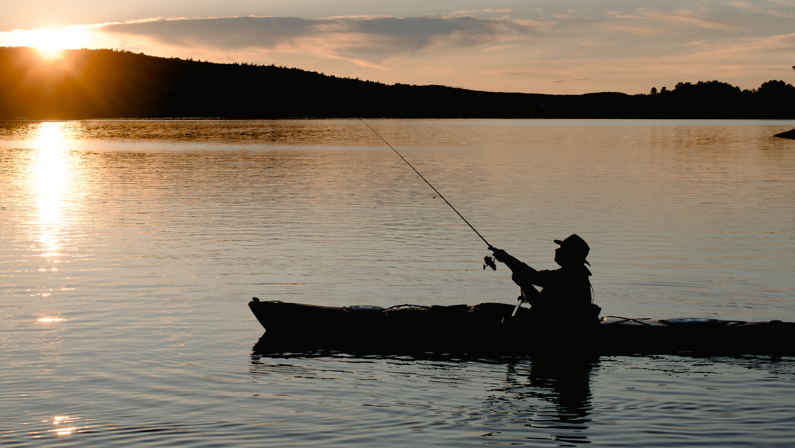 Man fishing in boat while the sun goes down.